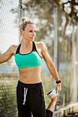 Athlete woman in sports clothing stretching at fence