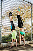 Mother and daughter (10-11) performing handstand at fence