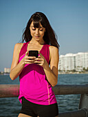 Frau in Sportkleidung schaut auf Smartphone auf Brücke