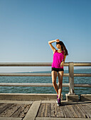 Frau in Sportkleidung steht an einem sonnigen Tag auf einer Brücke