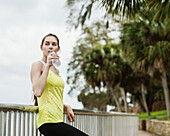 Vereinigte Staaten, Florida, Tampa, Frau in Sportkleidung lehnt an Zaun und trinkt Wasser aus Flasche 
