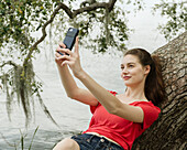 Lächelnde Frau macht ein Selfie auf einem Ast am Fluss