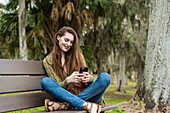 Lächelnde Frau sitzt auf einer Bank und schaut auf ihr Smartphone
