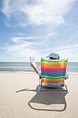 USA, Massachusetts, Cape Cod, Nantucket Island, Rear view of woman on colorful beach chair reading magazine on beach