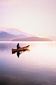 Vereinigte Staaten, New York, Frau paddelt Kanu auf dem Lake Placid bei Sonnenaufgang, Adirondacks State Park