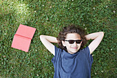 Junge mit Buch im Gras liegend und lächelnd