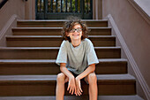 USA, New York, New York City, Junge sitzt auf den Stufen vor einem Gebäude