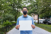 USA, New York, New York City, Porträt eines Mannes mit Gesichtsmaske, der ein leeres Schild in der Stadt hält
