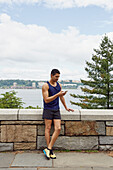 USA, New York, New York City, Mann in Sportkleidung schaut auf Smartphone an Mauer in Park