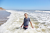 Lächelnder Junge (8-9) in den Wellen des Meeres