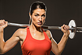 Studio portrait of athletic woman in red sleeveless top with barbell
