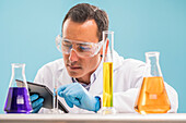 Scientist with digital tablet looking at yellow liquid in measuring beaker