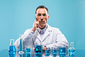 Porträt eines Wissenschaftlers mit Bechergläsern mit blauer Flüssigkeit im Vordergrund