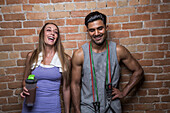 Lächelnder Mann und lächelnde Frau vor einer Mauer im Fitnessstudio