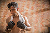 Mann ohne Hemd mit Boxhandschuhen und Handtuch im Fitnessstudio