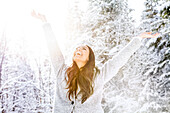 Happy woman with arms raised in snow covered forest