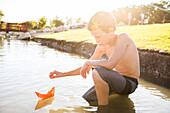 Shirtless boy (8-9) floating paper boat on river