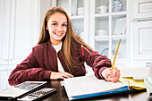 Portrait of smiling girl (12-13) doing homework at desk