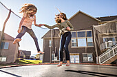 Mädchen (10-11, 12-13) springen auf dem Trampolin vor dem Haus