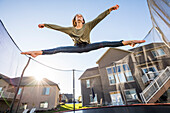 Mädchen (12-13) springt auf dem Trampolin vor dem Haus
