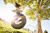 Smiling girl (12-13) on tire swing in garden