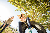 Smiling girls (10-11, 12-13) on tire swing in garden