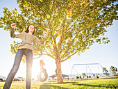 Girl (12-13) spinning hula hoop, sister (10-11) on tire swing in background