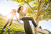 Girls (10-11, 12-13) playing with tire swing in garden