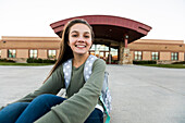 United States, Utah, Lehi, Portrait of smiling girl (12-13) sitting in front of school building