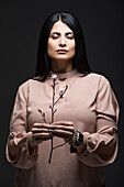 Studio-Porträt einer Frau, die mit geschlossenen Augen einen blühenden Zweig hält