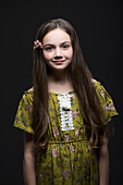 Studio-Porträt eines lächelnden Mädchens (10-11) in grünem Kleid mit Blume im Haar