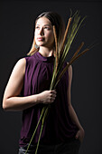 Studio portrait of woman in sleeveless purple top holding bunch of cattails