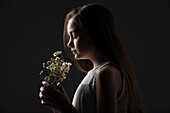 Profile of girl (10-11) holding bunch of wildflowers against black background
