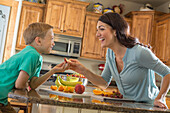 Mother and son (6-7) eating fruit in kitchen