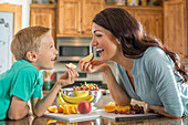 Mother and son (6-7) eating fruit in kitchen