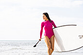 Frau im rosa Badeanzug trägt Paddelbrett am See