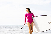 Woman in pink swimsuit carrying paddleboard by lake