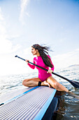 Woman in pink swimsuit sitting on paddleboard on lake