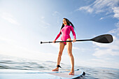 Woman in pink swimsuit standing on paddleboard on lake