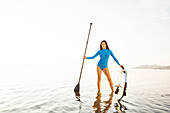 Frau im blauen Badeanzug, Ruder und Paddleboard im See haltend
