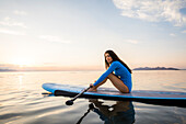 Porträt einer Frau im blauen Badeanzug auf einem Paddleboard auf einem See bei Sonnenuntergang