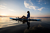 Frau in sitzend auf Paddleboard auf See bei Sonnenuntergang