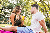 Paar sitzt auf einer Decke und unterhält sich bei einem Picknick im Park 