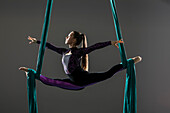 Young acrobat doing splits on aerial silks