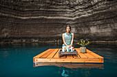 Beautiful woman kneeling on wooden raft on pond