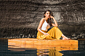 Schöne Frau sitzt auf einem Holzfloß auf einem Teich