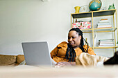 Frau sitzt auf dem Sofa und arbeitet an einem Laptop