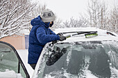 USA, New Mexico, Santa Fe, Frau mit Gesichtsmaske räumt Schnee aus dem Auto