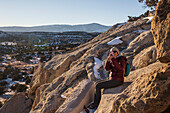 USA, New Mexico, Los Alamos, Bandelier national Monument, Tsankwai, Frau sitzt auf Felsen und fotografiert mit Smartphone