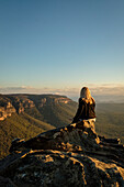 Australien, NSW, Blue Mountains National Park, Rückansicht einer Frau mit Blick auf die Aussicht im Megalong Valley bei Sonnenuntergang